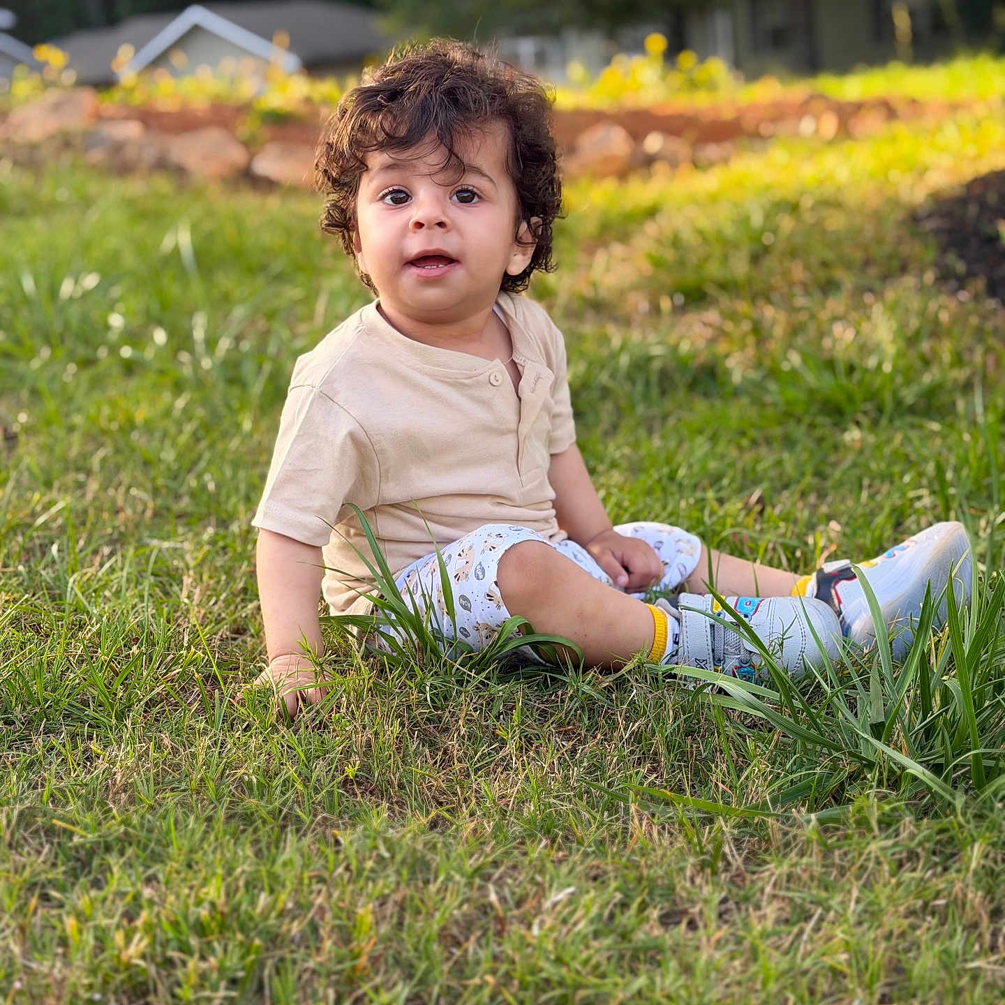 Ravaymaan joined the competition — help win amazing prizes! child, toddler, grass, outdoor, curly_hair, sitting, beige_shirt, patterned_shorts, sneakers, greenery, sunlight, garden, portrait, young_child, nature, daylight, casual_clothing, expression, background, house