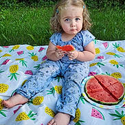 Addison joined the competition — help win amazing prizes! toddler, child, watermelon, blanket, outdoor, grass, curly_hair, blue_eyes, sitting, fruit, summer, snack, plate, nature, cute, clothing, patterned_blanket, picnic, expression, barefoot