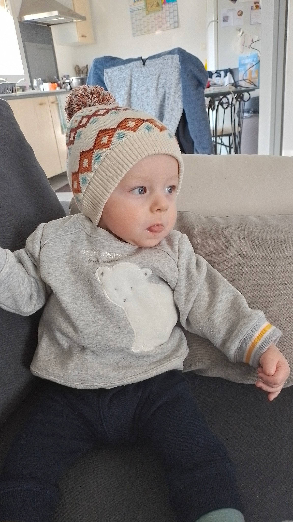 Charly a rejoint le concours — aidez-le/la à gagner de superbes lots ! baby, baby_toddler_clothing, beanie, cap, child, comfort, couch, fashion_accessory, flooring, grey, hat, headwear, knee, knit_cap, pattern, person, room, sitting, sleeve, t_shirt