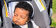 Zaydan is registered to the contest to win money with this photo: baby, car_seat, sleeping, curly_hair, pacifier, infant, child, sunlight, gray, seatbelt, outdoor, peaceful, cute, hands, face, head, portrait, person, resting, young