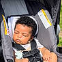 baby, car_seat, sleeping, curly_hair, pacifier, infant, child, sunlight, gray, seatbelt, outdoor, peaceful, cute, hands, face, head, portrait, person, resting, young