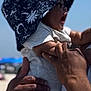 baby, child, hat, sun_hat, adult_hand, beach, outdoor, sky, summer, holding, close_up, person, infant, happy, daylight, casual_clothing, skin, portrait, nature, vacation