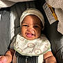 baby, smile, car_seat, bib, hat, infant, child, happy, seatbelt, closeup, indoors, clothing, safety, cute, young_child, portrait, baby_accessory, blanket, infant_face, baby_smiling