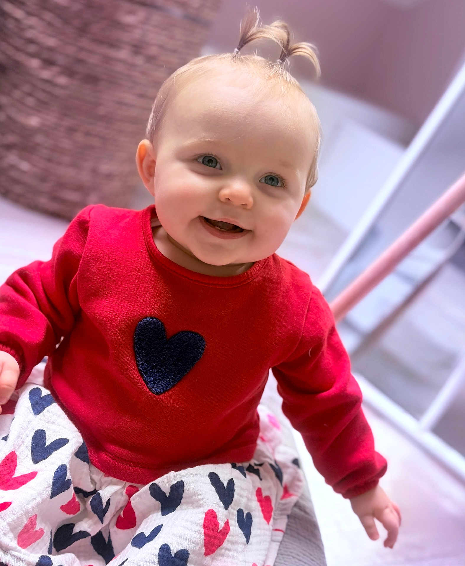 Këyla participe au concours pour gagner de l'argent avec cette photo : baby, child, smile, face, portrait, red_sweater, heart_pattern, skirt, pony_tail, blond_hair, blue_eyes, indoors, soft_lighting, closeup, playful, happy, candid, blanket, nursery_furniture, seated