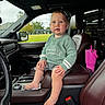 toddler, child, baby, car_interior, seat, leather_seat, sweater, barefoot, drool, center_console, pink_tumbler, window, daylight, green_sweater, curious_expression, head, face, hand, foot, seatbelt