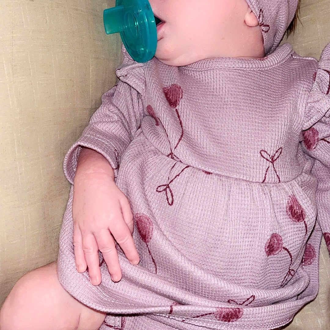Aurora joined the competition — help win amazing prizes! baby, infant, child, portrait, sitting, pacifier, headband, pink_outfit, floral_pattern, dress, romper, cushion, sofa, indoor, closeup, face, hand, legs, socks, sleepy