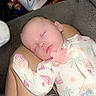 baby, infant, sleeping, pacifier, onesie, portrait, indoors, couch, lap, person, face, closed_eyes, peaceful, sitting, tattoo, clothing, household_items, snacks, cup, photograph