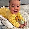 baby, child, yellow_clothing, smiling, happy, toy, blanket, quilt, indoors, face, portrait, cute, infant, hands, hair, lying_down, cozy, playful, expression, skin