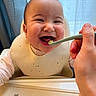 Yoona is registered to the contest to win money with this photo: baby, child, feeding, high_chair, bib, spoon, smiling, happy, indoor, person, face, hand, curtain, light, cute, infant, expression, clothing, table, meal