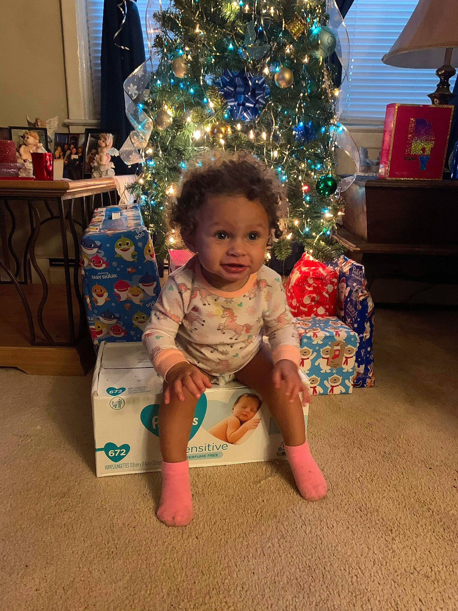 Ryleigh is registered to the contest to win money with this photo: baby, baby_toddler_clothing, christmas, christmas_ornament, christmas_tree, event, eye, face, fun, happy, head, holiday, holiday_ornament, human_body, lap, living_room, person, sitting, toddler, tree