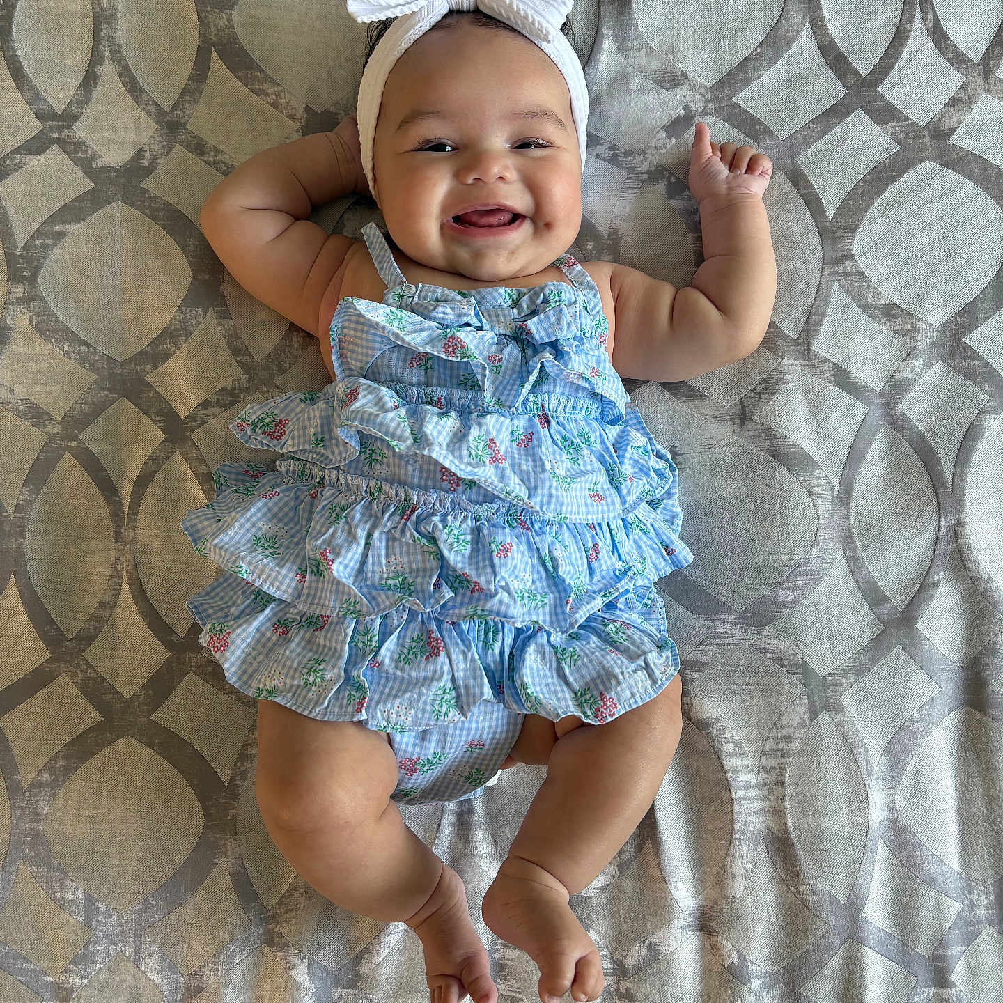 Zoe is registered to the contest to win money with this photo: baby, blue, bow, cheeks, child, cute, dress, fabric, hands, happy, headband, indoors, infant, legs, lying_down, patterned_background, skin, smiling, toes, white