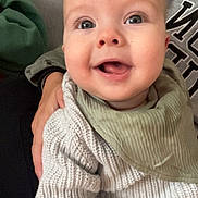 Hunter is registered to the contest to win money with this photo: baby, smiling, indoor, person, knit_sweater, green_bib, happy, face, child, closeup, portrait, seated, hand, casual_clothing, cozy, couch, skin, head, infant, cute