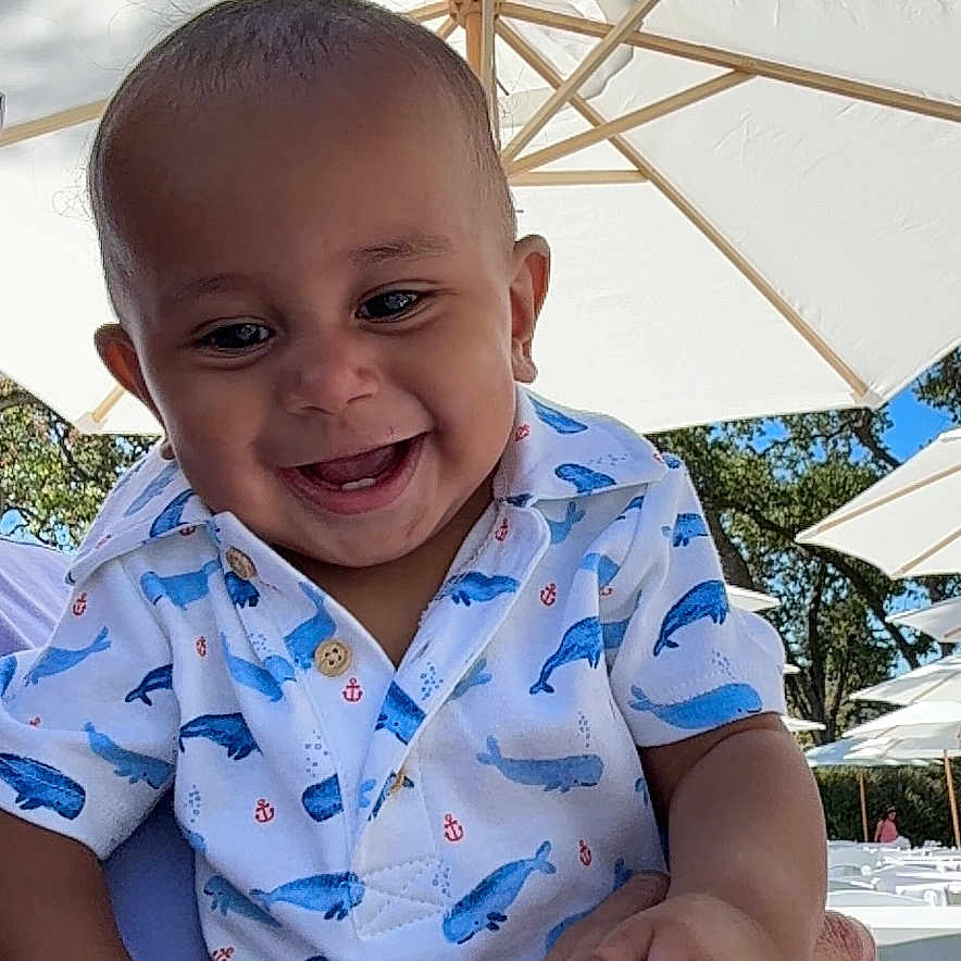 Romeo Jr is registered to the contest to win money with this photo: baby, blue_sky, casual_clothing, cheerful, child, daylight, family, hand, happy, holding, infant, nature, outdoor, person, shirt, smiling, sunny, trees, umbrella, whale_pattern