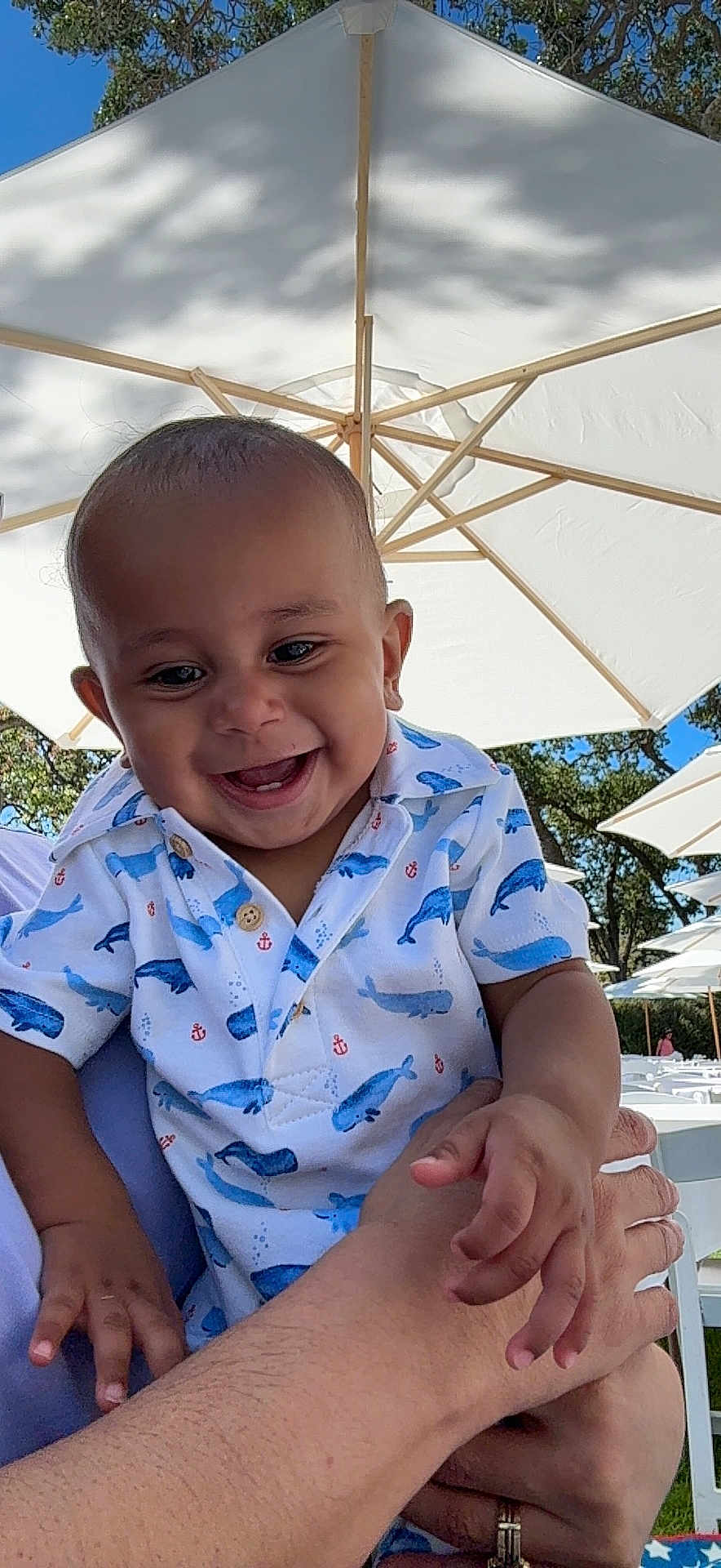 Romeo Jr is registered to the contest to win money with this photo: baby, child, smiling, happy, outdoor, umbrella, shirt, whale_pattern, person, hand, trees, daylight, sunny, nature, family, holding, blue_sky, casual_clothing, infant, cheerful
