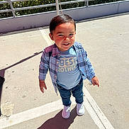 Carlos is registered to the contest to win money with this photo: child, toddler, boy, outdoor, sunny, plaid_shirt, blue_tshirt, best_brother, jeans, white_sneakers, smiling, shadow, concrete, parking_lot, railing, plants, daylight, casual_clothing, happy, standing