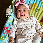 Merry is registered to the contest to win money with this photo: baby, baby_seat, bird, child, clothing, colorful, cute, gold_hearts, happy, headband, indoors, infant, laying_down, patterned, pink_bow, portrait, smiling, snail, toddler, white_dress