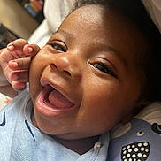 Amir is registered to the contest to win money with this photo: baby, smiling, close_up, face, child, infant, happy, blue_clothing, hand, skin, eyes, mouth, cheeks, soft_toys, fabric, indoor, portrait, cute, expression, cozy