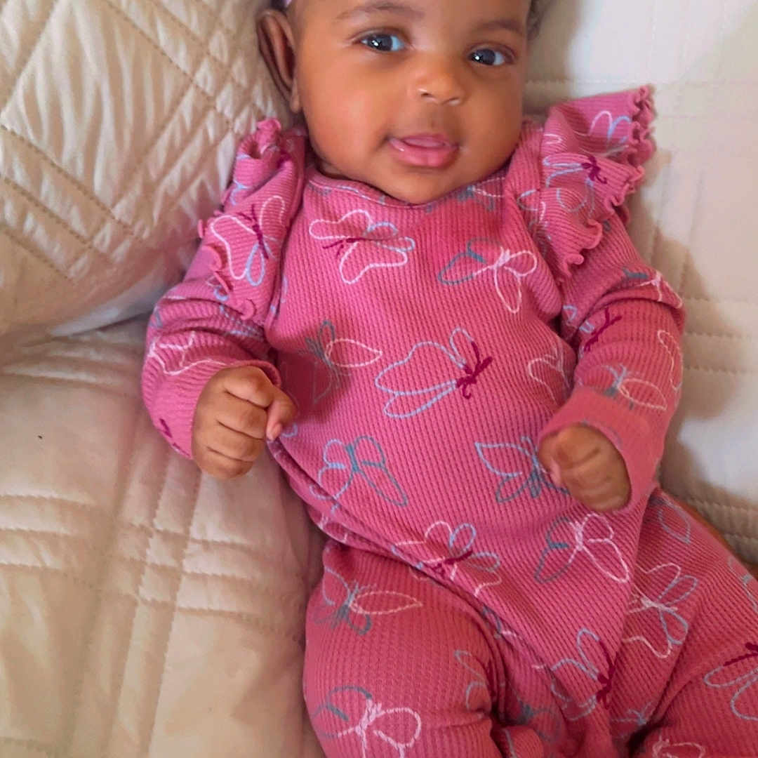 Mayika is registered to the contest to win money with this photo: baby, butterfly_pattern, child, comfortable, couch, cute, flower, happy, headband, indoors, infant, pink_clothing, portrait, quilted_blanket, relaxed, sitting, smiling, soft_toys, white_socks, young_child