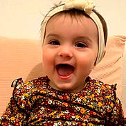 Lëannah a rejoint le concours — aidez-le/la à gagner de superbes lots ! baby, background, cheerful, child, clothing, cute, expression, face, flower_pattern, happy, headband, headwear, indoors, infant, person, portrait, sitting, smiling, warm_colors, young_child