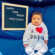 Preeyansh is registered to the contest to win money with this photo: baby, infant, child, onesie, bed, blue_bedspread, letter_board, text, celebration, milestone, happy, cute, indoors, light_and_shadow, wood_panel, smiling, face, feet, person, clothing