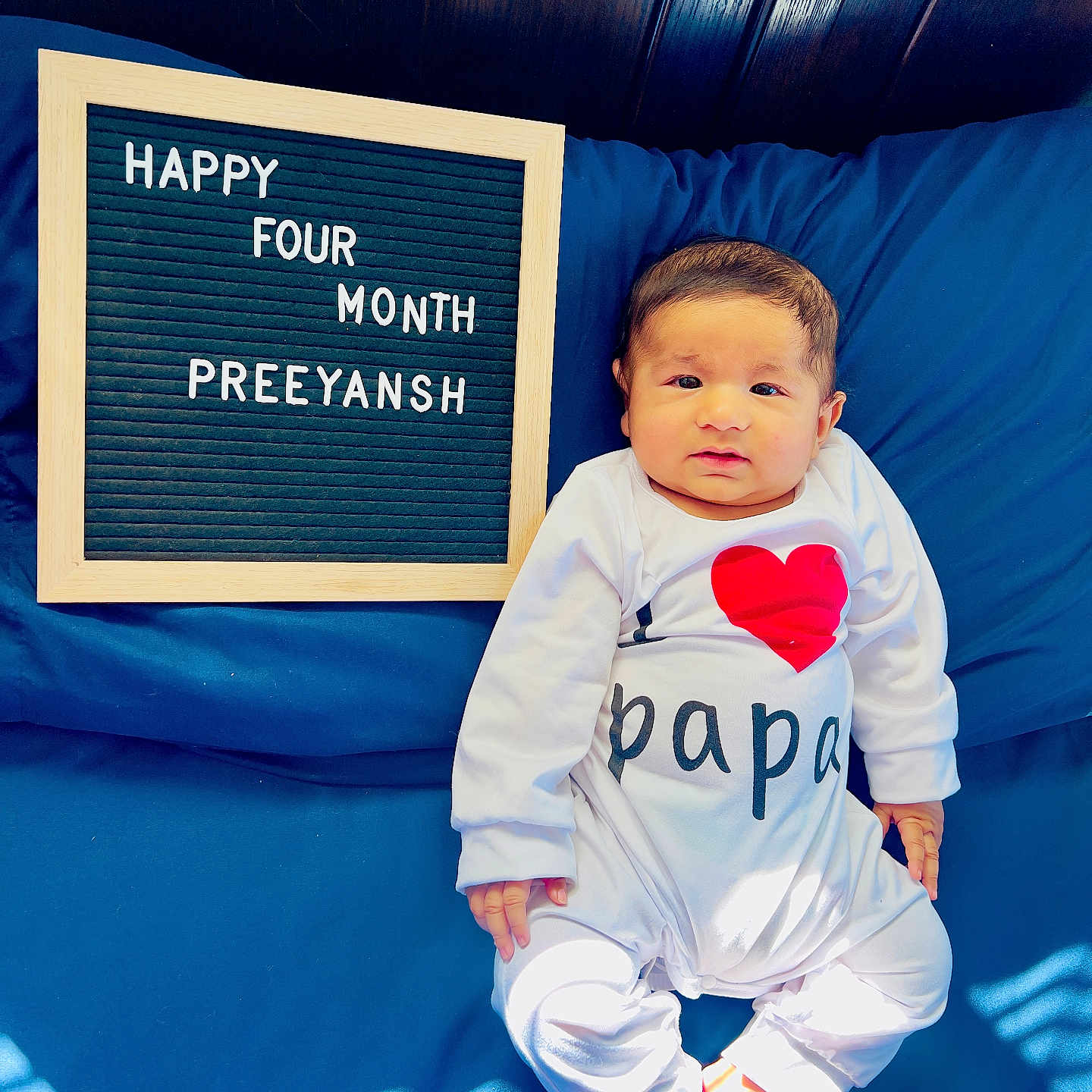 Preeyansh is registered to the contest to win money with this photo: baby, infant, child, onesie, bed, blue_bedspread, letter_board, text, celebration, milestone, happy, cute, indoors, light_and_shadow, wood_panel, smiling, face, feet, person, clothing