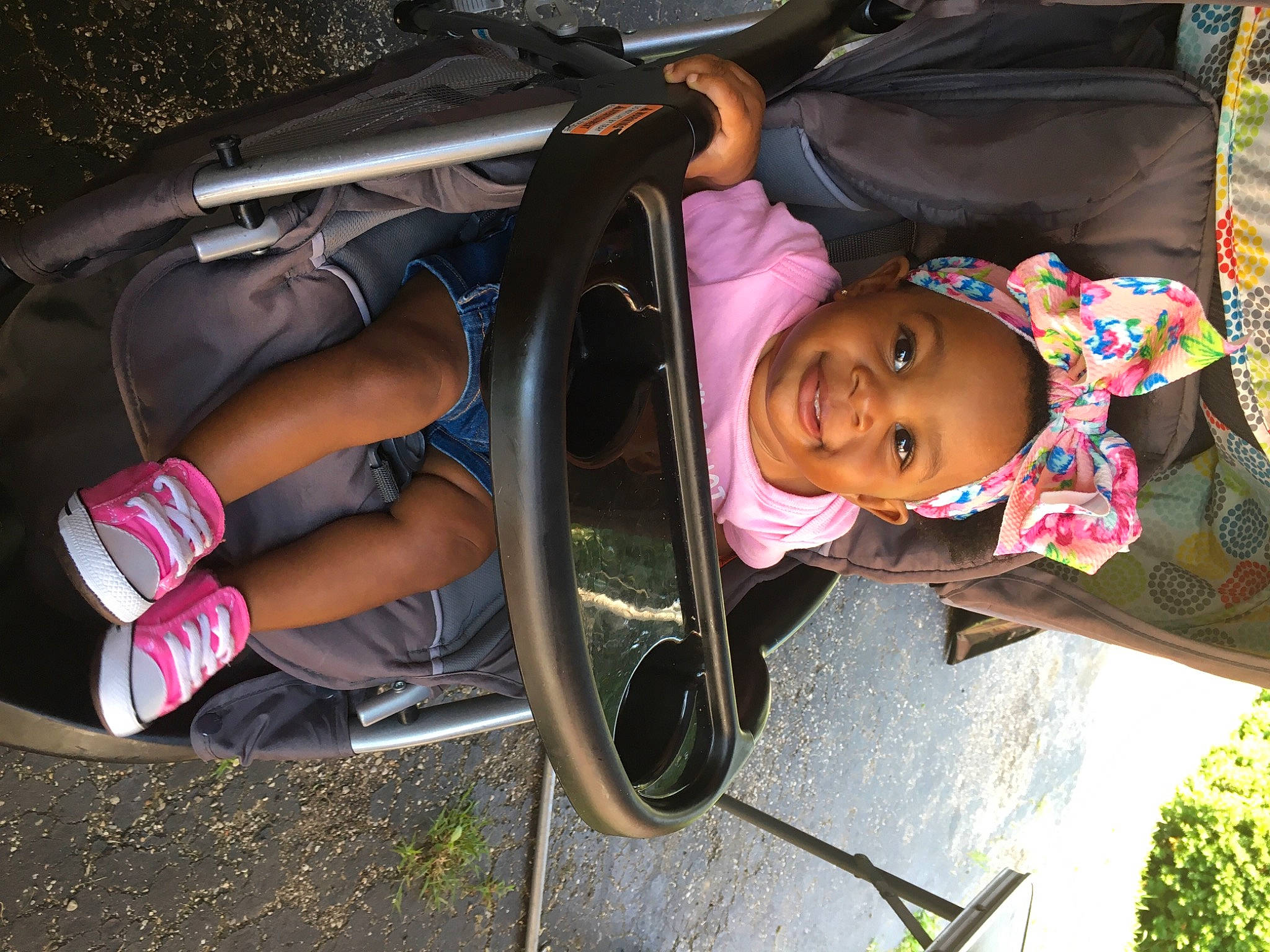 Imani is registered to the contest to win money with this photo: auto_part, automotive_exterior, automotive_lighting, automotive_tire, bumper, child, fun, grass, joy, leisure, light, motor_vehicle, person, pink, plant, public_space, recreation, smile, toddler, tree