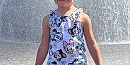 Lucy is registered to the contest to win money with this photo: child, girl, smiling, water_fountain, wet_hair, sunlight, outdoor, clothing, shorts, tank_top, disney_characters, happy, standing, pavement, summer, playful, daytime, person, cute, casual