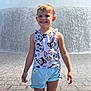 child, girl, smiling, water_fountain, wet_hair, sunlight, outdoor, clothing, shorts, tank_top, disney_characters, happy, standing, pavement, summer, playful, daytime, person, cute, casual