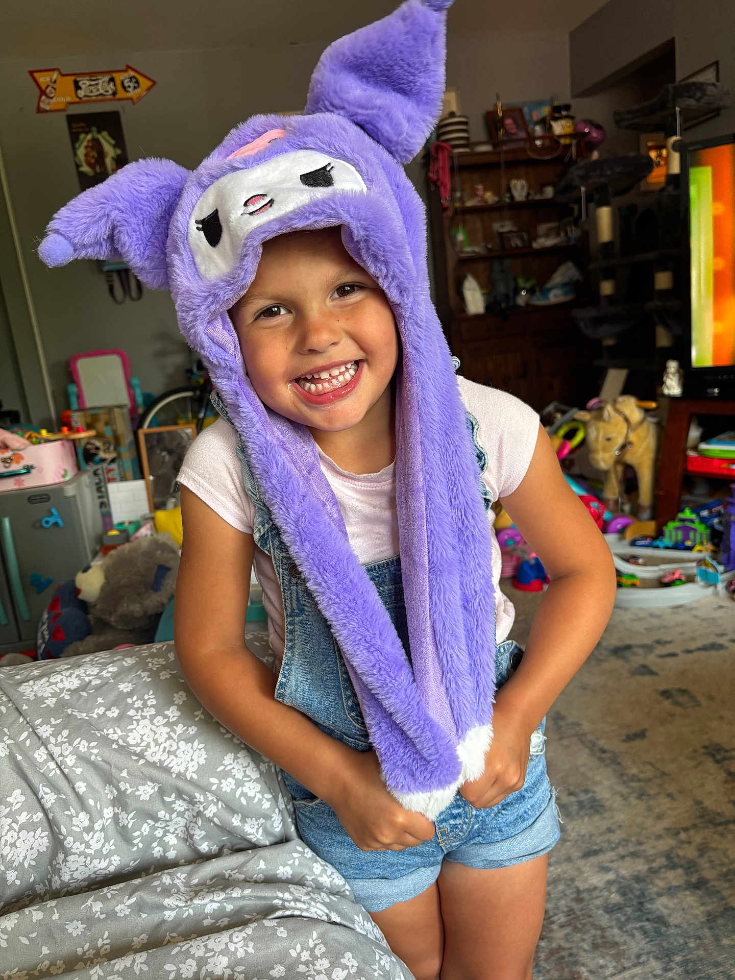 Lucy joined the competition — help win amazing prizes! child, smiling, purple_hat, plush_hat, living_room, toys, shorts, tshirt, happy, indoor, furniture, television, carpet, shelf, decor, person, cute, playful, portrait, kid