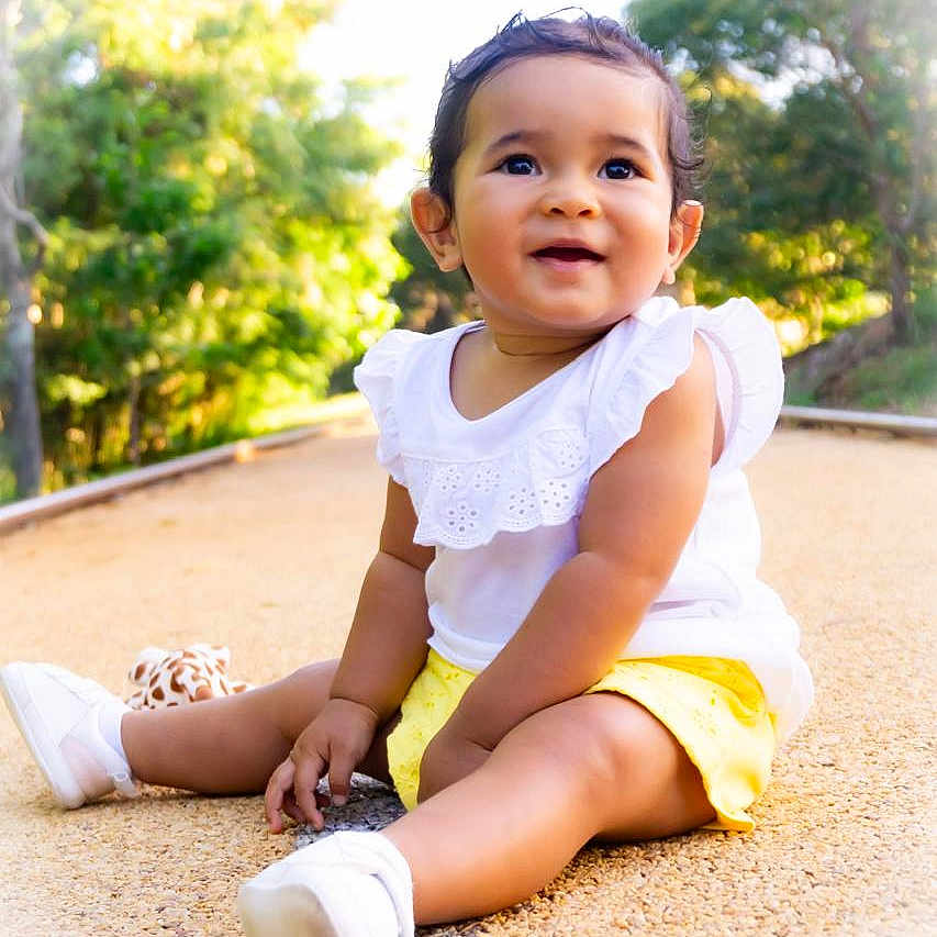Anayah participe au concours pour gagner de l'argent avec cette photo : baby, child, cute, daylight, footwear, giraffe_plush, gravel_path, greenery, happy, nature, outdoor, portrait, sitting, smiling, sunlight, toddler, toy, trees, white_top, yellow_shorts