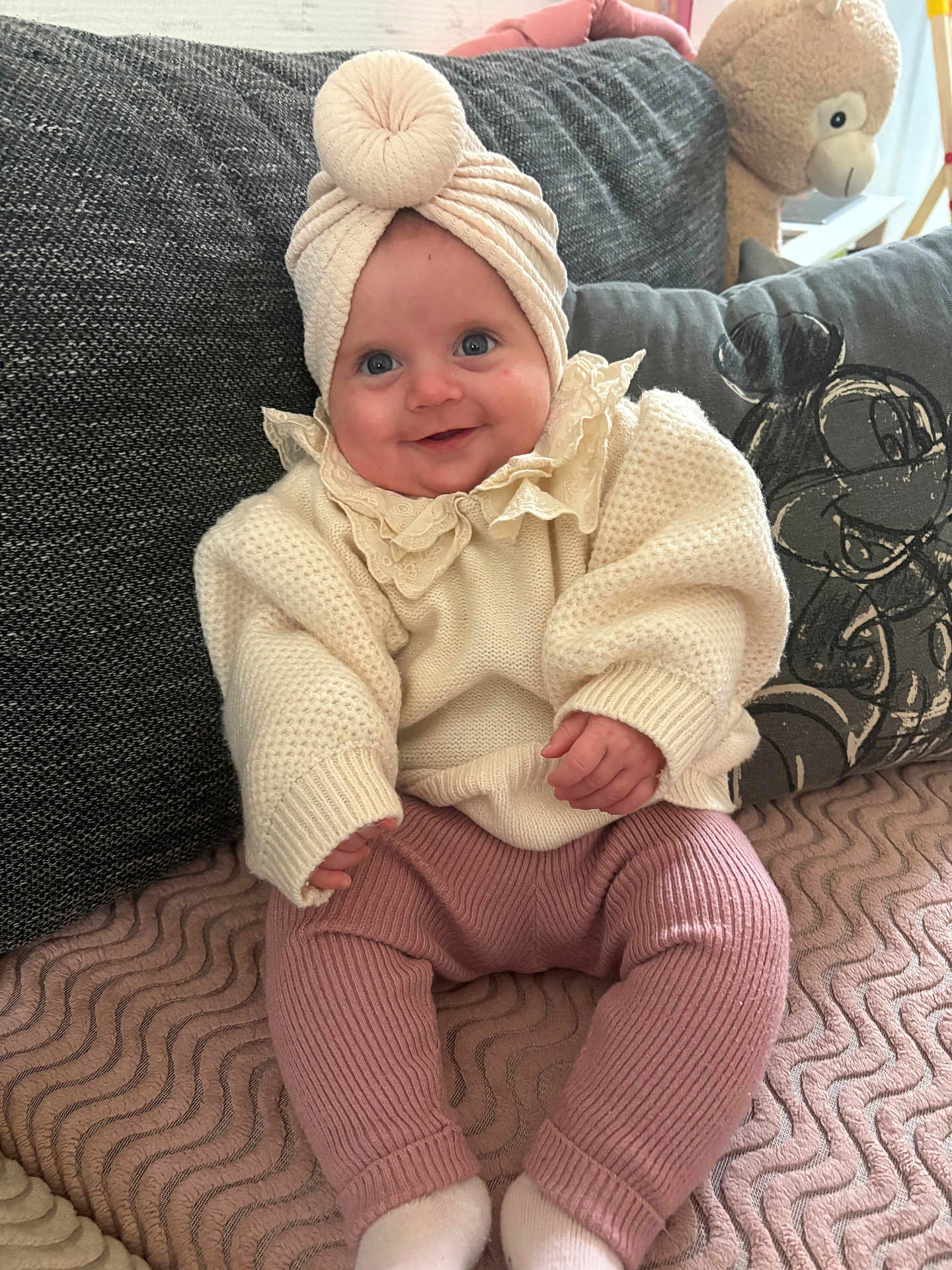 Melynda participe au concours pour gagner de l'argent avec cette photo : baby, infant, smiling, blue_eyes, turban, headwrap, knit_sweater, ruffle_collar, pink_leggings, socks, couch, cushion, plush_toy, stuffed_animal, monkey_toy, blanket, indoor, portrait, cozy, happy