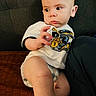 baby, child, infant, tshirt, diaper, couch, furniture, person, skin, hand, face, eyes, sitting, indoors, curious, expression, clothing, leg, footwear, background