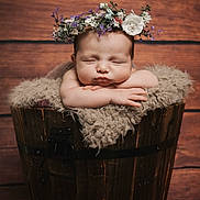 Emerald is registered to the contest to win money with this photo: arms, baby, child, closeup, cute, face, flower_crown, fluffy_blanket, hands, head, infant, newborn, peaceful, portrait, resting, sleeping, soft_texture, studio_photo, wood_background, wooden_bucket