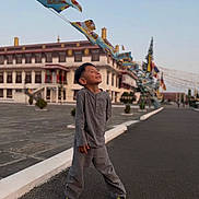 Loden a rejoint le concours — aidez-le/la à gagner de superbes lots ! boy, building, casual, child, colorful, daylight, flag_banners, flags, grey_clothing, happy, joyful, outdoor, pavement, sky, smiling, standing, street, traditional_architecture, urban, yellow_shoes