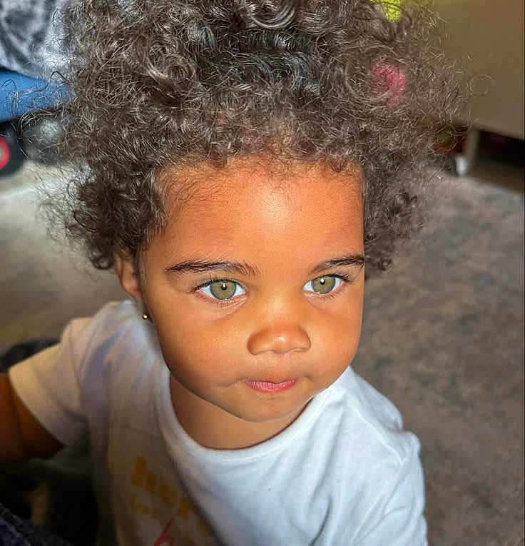 Lia a rejoint le concours — aidez-le/la à gagner de superbes lots ! child, toddler, curly_hair, green_eyes, portrait, face, skin, earrings, white_shirt, indoor, closeup, expression, cute, young_child, person, natural_light, thoughtful, baby, head, eyebrows