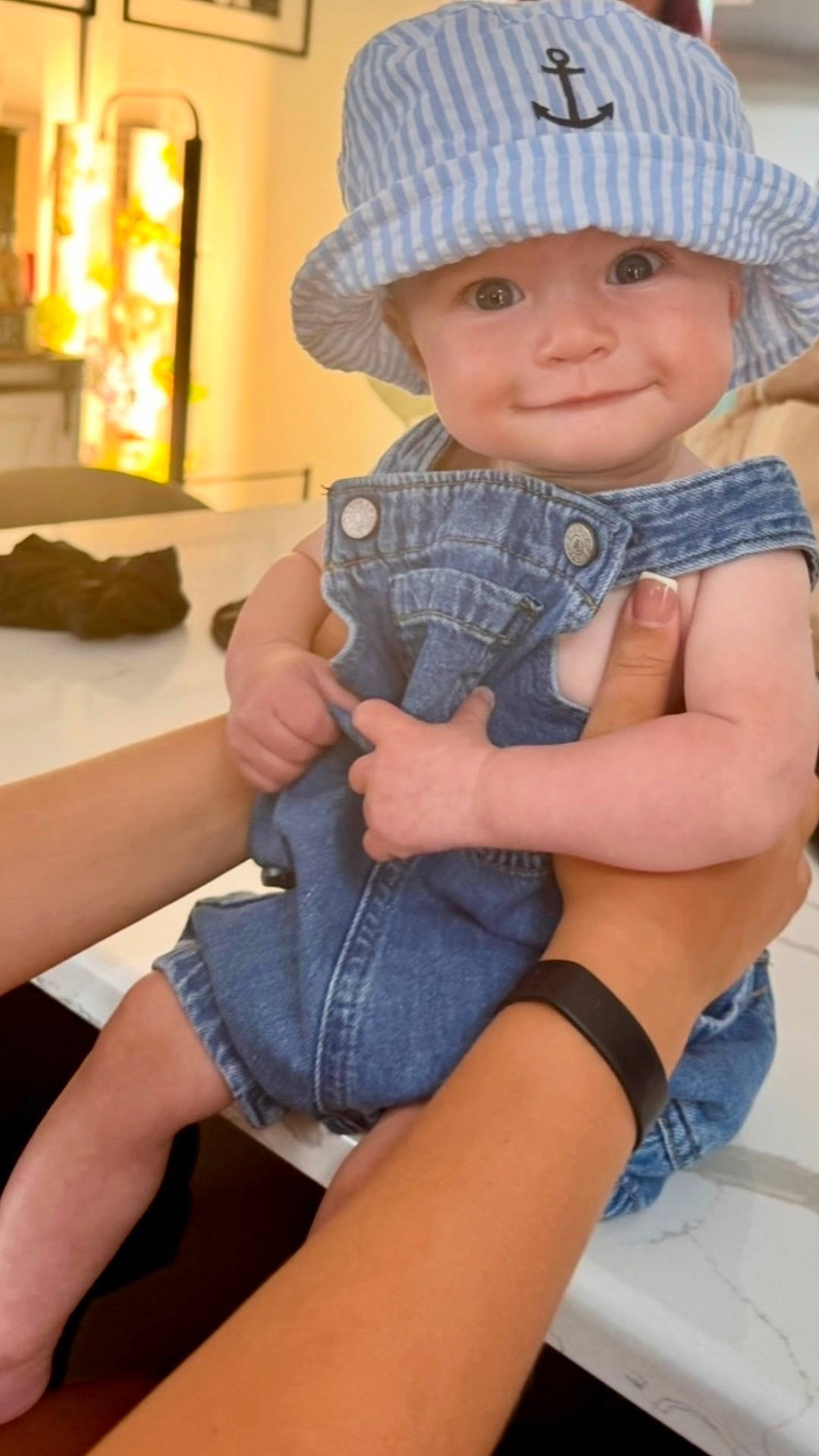 Luca is registered to the contest to win money with this photo: arm, baby, blue_hat, bucket_hat, cheeks, child, clothing, cute, denim_overalls, face, hands, happy, holding, indoor, infant, marble_countertop, person, skin, smile, table