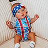 baby, infant, headband, stars_and_stripes, blue_eyes, sitting, plush_chair, cream_color, clothing, sock, cute, portrait, indoor, comfortable, furniture, small_hands, expression, child, new_york_rangers, patterned_clothing