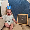 baby, infant, crown, chair, blanket, letter_board, smile, happy, milestone, sitting, clothing, striped_shirt, foot, hand, indoor, portrait, cute, child, celebration, home