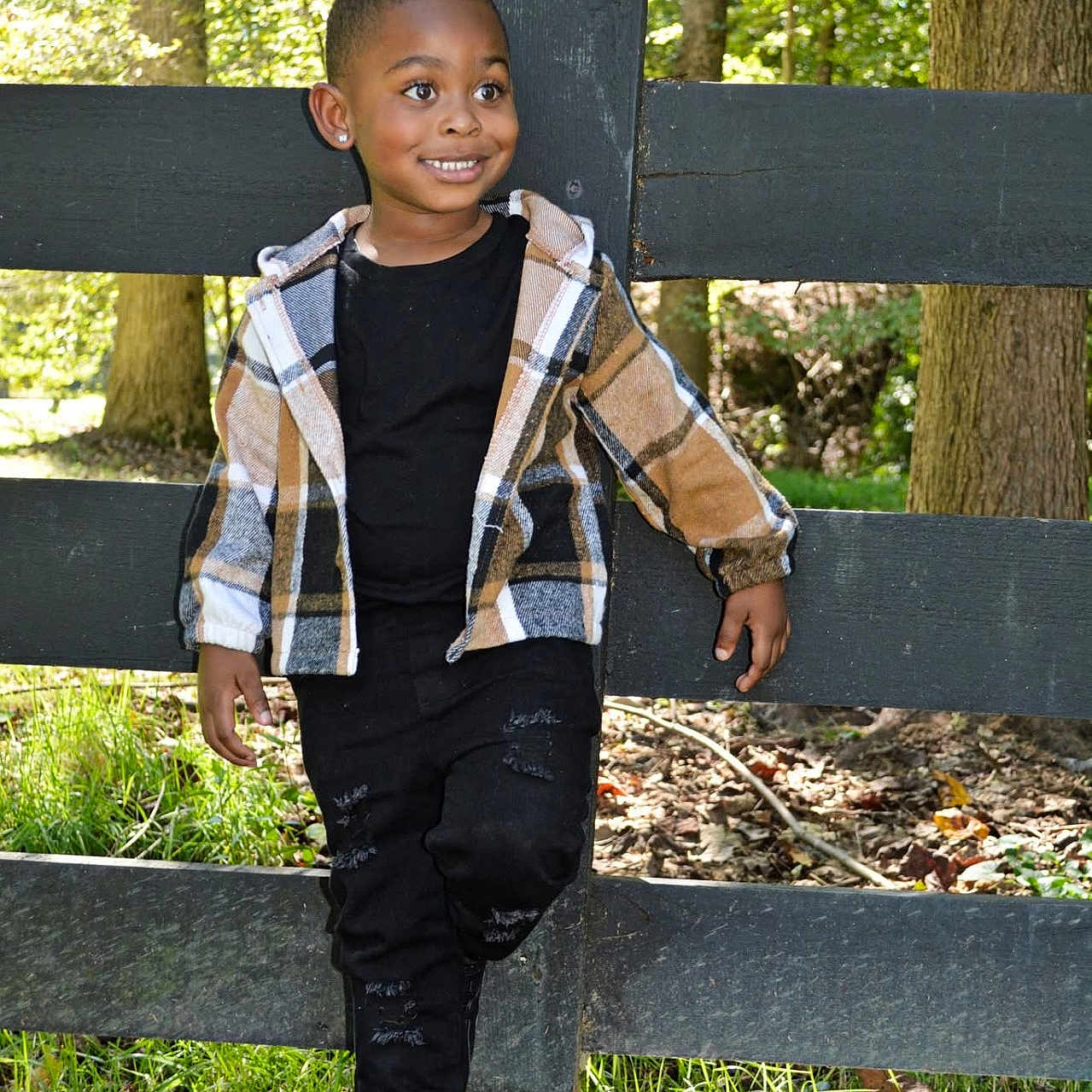 Judaerion is registered to the contest to win money with this photo: child, boy, smiling, plaid_jacket, black_clothing, outdoor, fence, grass, trees, forest, nature, sunlight, casual_pose, earrings, happy, portrait, young, person, leisure, daylight