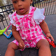 Harmony is registered to the contest to win money with this photo: toddler, child, headband, bow, romper, pink_clothing, toy_car, outdoor, table, metal_table, sitting, curious, cute, baby_shoes, footwear, person, daytime, play, expression, casual