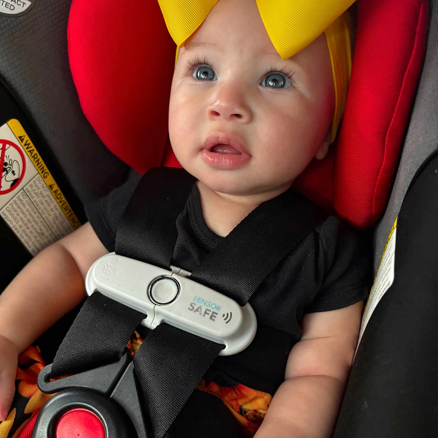 Xaviah is registered to the contest to win money with this photo: adorable, baby, baby_girl, black_clothing, blue_eyes, car_seat, child, closeup, cute, expression, headwear, indoor, infant, person, portrait, red_cushion, safety_harness, seat, seatbelt, yellow_bow