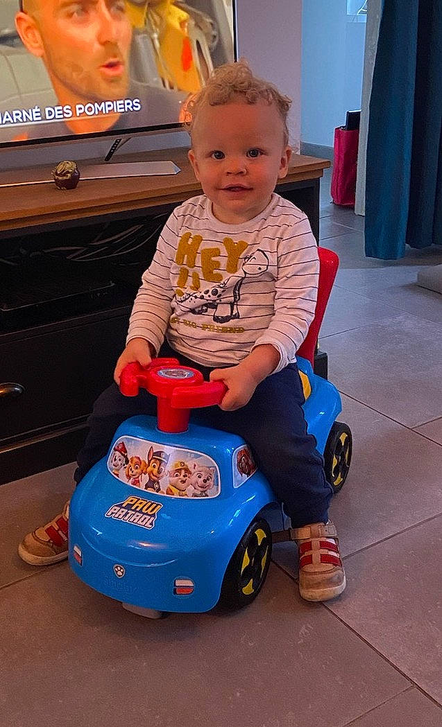 Aïden a rejoint le concours — aidez-le/la à gagner de superbes lots ! automotive_design, baby, baby_toddler_clothing, baby_toys, car, child, electric_blue, flooring, fun, happy, headwear, joy, motor_vehicle, orange, person, riding_toy, sitting, smile, tire, toddler