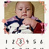 baby, baby_card, blue, child, clothing, doodle, eyes, face, floral_frame, indoor, infant, lying_down, milestone_photo, photocollage, pink, portrait, serious_expression, sitting, sports_jersey, three_months