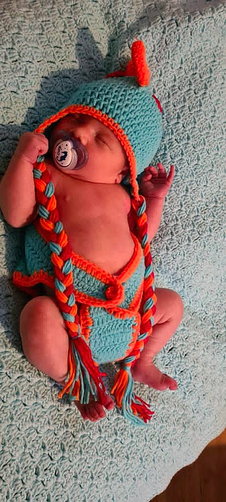 Louie is registered to the contest to win money with this photo: cap, doll, eye, fashion_accessory, fawn, hand, headwear, jewellery, lip, magenta, neck, orange, pattern, peach, person, personal_protective_equipment, pink, red, textile, toy