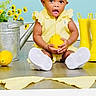 baby, child, yellow_clothing, headband, lemon, rain_boots, watering_can, flowers, floor, indoor, gown, white_shoes, gingham_cloth, cute, portrait, sitting, bright_colors, happy, expression, studio