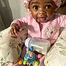 Kimora joined the competition — help win amazing prizes! baby, child, pink_onesie, bonnet, toy, milk_bottle, cushions, floral_pattern, indoor, cute, smiling, face, hands, sitting, infant, playful, comfort, expression, person, portrait