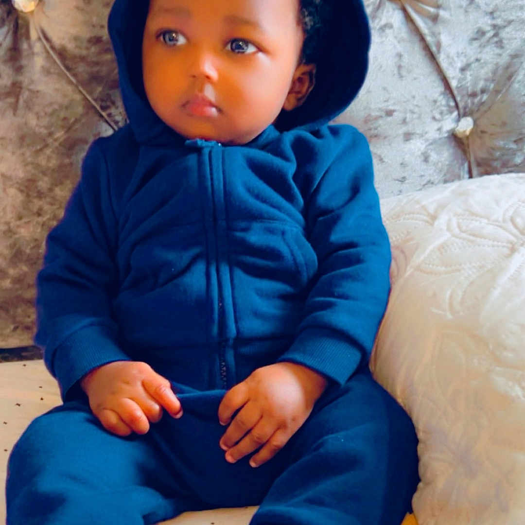 Aizeyosabor joined the competition — help win amazing prizes! bed, blue_hoodie, casual_clothing, child, cozy, curly_hair, cute, face, headboard, indoor, person, pillow, portrait, resting, shoes, sitting, soft_furniture, thoughtful, toddler, young_child