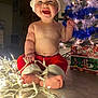 baby, child, christmas, holiday, lights, santa_hat, red_pants, smiling, indoors, floor, decorated_tree, gift_box, festive, cute, toes, holiday_decor, joyful, celebration, toddler, christmas_tree