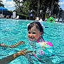 Naomi joined the competition — help win amazing prizes! child, toddler, swimming_pool, water, floaties, hair_bow, smiling, summer, sunny, outdoor, adult_hands, recreation, playful, blue_sky, trees, fence, swimwear, fun, happy, leisure