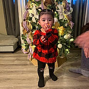 Naomi joined the competition — help win amazing prizes! toddler, child, christmas_tree, holiday_decorations, red_dress, black_tights, indoor, flooring, curtains, chair, snack, pigtails, smiling, person, family, festive, cozy, lighting, home, cute